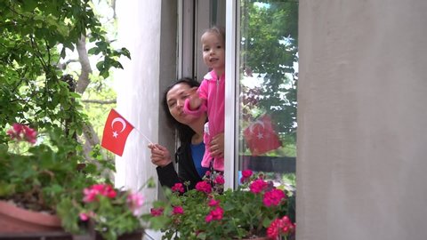 Turkish family mother and little girl child on balcony / window are smiling and waving the flag of Turkey. Self-isolation in quarantine, lockdown, stay at home, social distancing, coronavirus