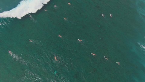 AERIAL, TOP DOWN: Massive barrel wave crashes and splashes over surfers paddling out. Flying above a big group of surfers getting ready to catch and ride big ocean waves in the stunning Maldives.