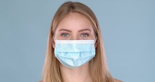 Young woman posing in medical face mask. Looking at camera with smile behind. Isolated on blue background. COVID19 concept. Slow motion video