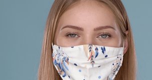 Close up portrait of beautiful woman wearing stylish face mask. Protection against viruses, pollution and dust. Isolated on blue background. Slow motion video