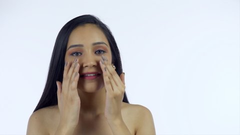 Pretty Indian girl applying cream on her happy face - beauty and skincare concept. Closeup shot of a young female happily following her skincare routine by gently massaging lotion on her face 