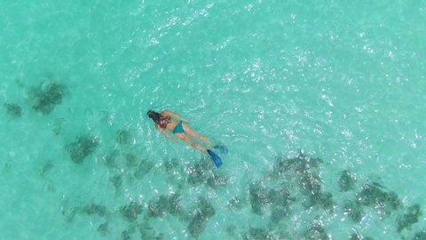 AERIAL, TOP DOWN: Young female tourist on an active summer vacation in the Maldives snorkels around the turquoise ocean. Woman snorkels around the shallows and explores the recovering coral reef.