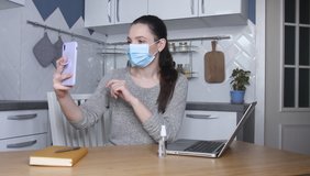 Young woman blogger wearing protective face mask recording video on mobile phone. Female blogger streaming about prevention spread of virus, using mask and Sanitizer spray.  Self quarantine