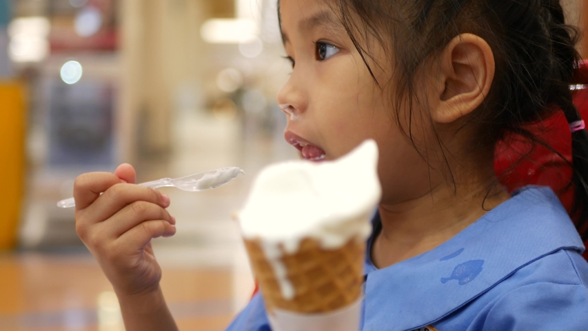 Close up of little Asian baby girl enjoys eating ice cream cone by herself | Shutterstock HD Video #1052088265