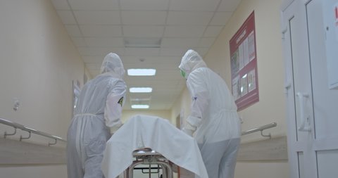 Doctors in protective suits carry the patient on a stretcher along the corridor of the clinic. Hospitalization of a sick patient on a stretcher.