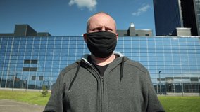 Video footage 4k, a mature man in a black protective mask puts on a protective transparent visor on his face on a city street on a sunny day