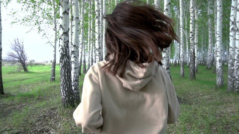 A young woman runs through a birch forest in slow motion. The girl runs between the trees. Back view.