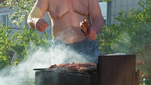 Fat funny man cooks kebabs and dances in the backyard. Unrecognizable man fries meat against the background of nature. The concept of gluttony and an idle lifestyle