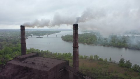 High chimneys of industrial plants smoke against background of nature, river, forest, islands. Dirty factory chimneys blow huge puffs of smoke into air. environmental poisoning by chemical industry.