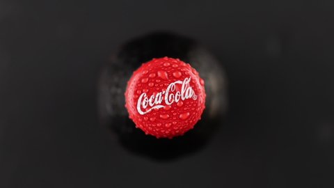 Minsk, Belarus, 05.2020 wet red cap of glass bottle with coca-cola logo rotating and stopping top view. cold jug is fogged up and water droplets running down. carbonated drink and black background