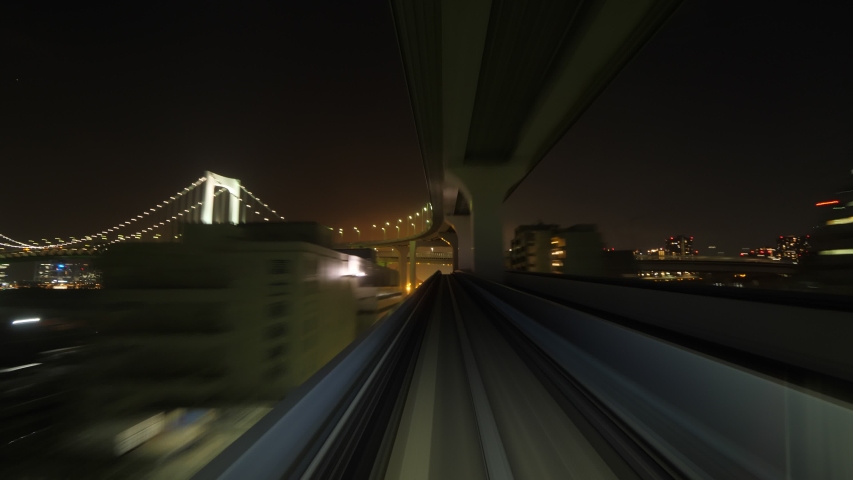 Modern automated metro line of Tokyo, cabin view timelapse at night, car make round turn and pass bridge. Accelerated shot with fine front perspective, outdoors seen in motion blur Royalty-Free Stock Footage #1052124331