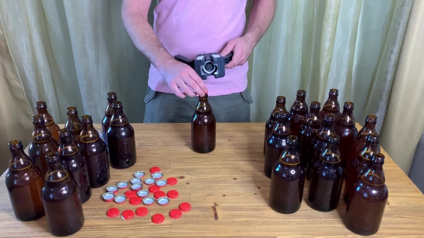 Craft beer brewing at home, man closes brown glass beer bottles with plastic capper on wooden table with red crown caps. Close up horizontal HD stock video. | Shutterstock HD Video #1052126008