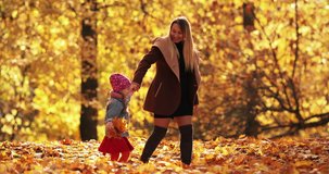 Pretty little girl in black jacket smiles and rejoices in the autumn park with her happy mum
