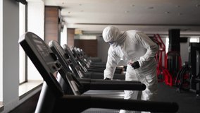 Hazmat worker disinfects gym fitness equipment from coronavirus covid-19 hazard with antibacterial sanitizer sprayer on quarantine. Man in protective suit cleans training apparatus at workout area. - Powered by Shutterstock - Get 15% off with code: PIKWIZARD15