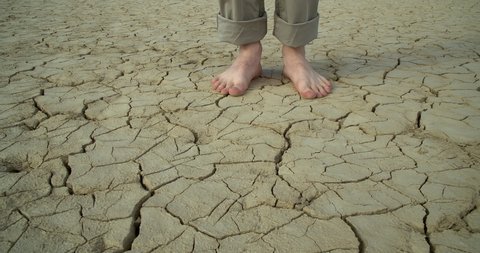 A young man walks barefoot on dry, cracked ground . Slow-motion close-up.