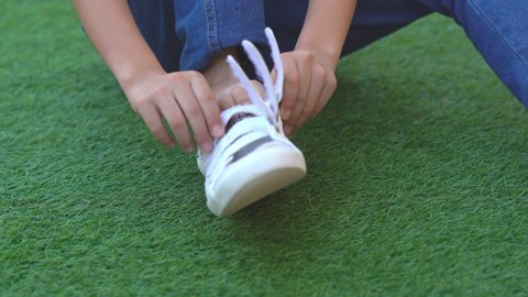 Close up legs and shoes kids wearing shoes for workout on grass field on home, asian child use white shoes for safety to playing and joyful on relaxing time, children warm up body for good halthy