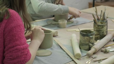 A teenage brunette girl sculpts a mug of clay, makes notches for the connection. Children's or family clay modeling workshop. Ceramic workshop