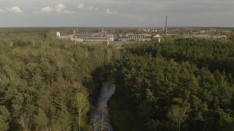 Aerial view - A forest and the river with the factory in the background in the sunset