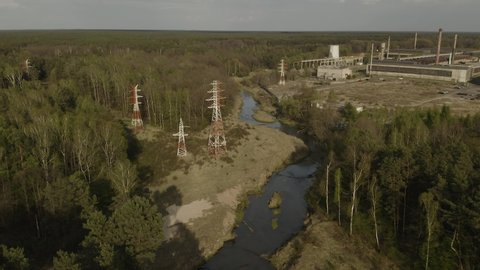 Aerial View - Powerlines in the forest over the river with factory in the background during sunset
