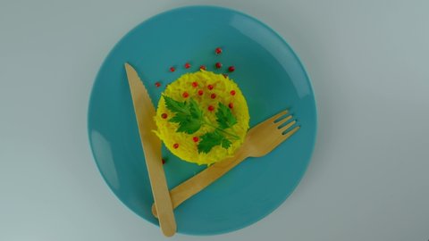 yellow vegetarian rice dish n atale with a touch of red pepper and green leaf, simplicity of the dish, on a plate with organic wooden forks and a knife. 