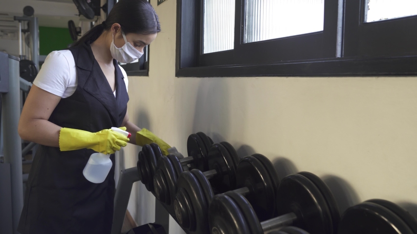 woman worker disinfects gym fitness equipment from coronavirus covid-19 with antibacterial sanitizer sprayer on quarantine. Cleaner in protective mask cleans training apparatus at workout area.
 Royalty-Free Stock Footage #1052158987