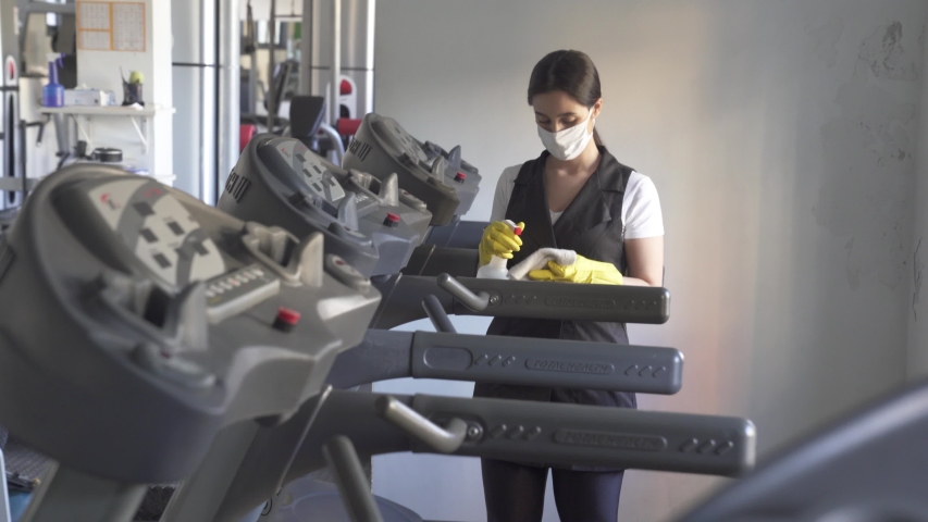 woman worker disinfects gym fitness equipment from coronavirus covid-19 with antibacterial sanitizer sprayer on quarantine. Cleaner in protective mask cleans training apparatus at workout area.
 Royalty-Free Stock Footage #1052159035