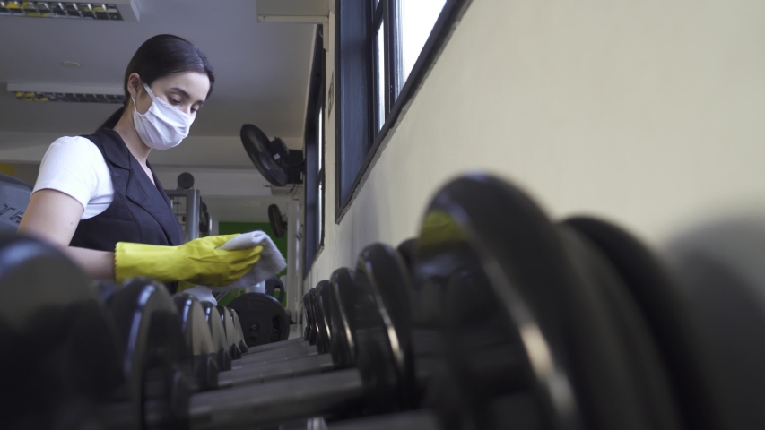 woman worker disinfects gym fitness equipment from coronavirus covid-19 with antibacterial sanitizer sprayer on quarantine. Cleaner in protective mask cleans training apparatus at workout area.
 Royalty-Free Stock Footage #1052159179