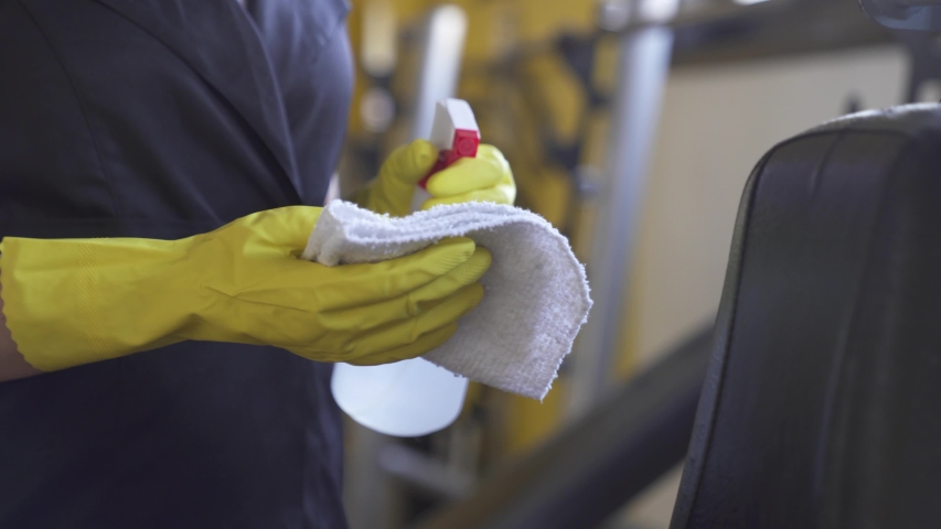 woman worker disinfects gym fitness equipment from coronavirus covid-19 with antibacterial sanitizer sprayer on quarantine. Cleaner in protective mask cleans training apparatus at workout area.
 Royalty-Free Stock Footage #1052159185