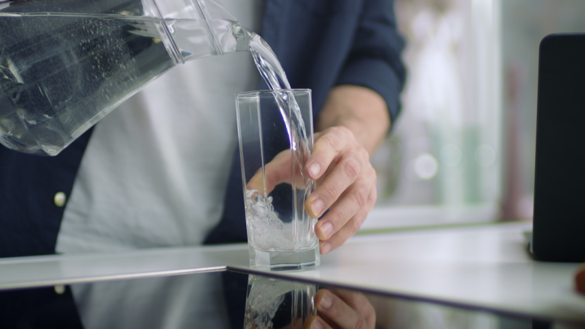 Closeup male hands pouring water into glass from jug at kitchen background. Unrecognizable person drinking water at home kitchen. Unknown man standing in modern home alone. | Shutterstock HD Video #1052159635