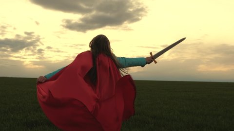 children fight with toy sword. happy childhood concept. free girl in a red cloak runs with swords in his hand across field playing medieval knight. young girl playing super heroes. child play knights.