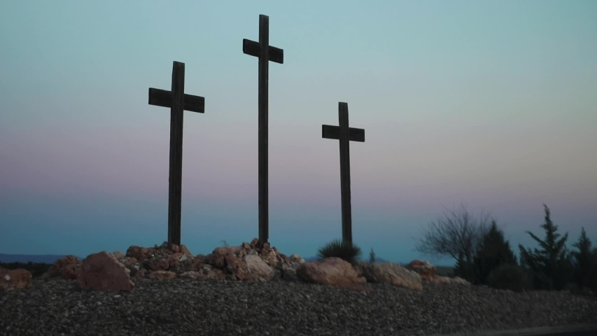 Three wooden crosses stand outside of a church and cemetery ahead of Easter as the sun sets in the desert countryside.