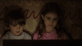Portrait Сute Little Kids While Watching TV on Laptop. Boy and Girl Watch Cartoon on Laptop on Living Room. Concept Video Game, Entertainment, Emotions, Family. Children Brother and Sister Watching TV
