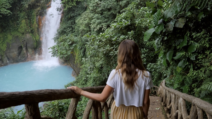 Young woman contemplating turquoise waterfall in Costa Rica going down the stairs and watching beauty in nature  Royalty-Free Stock Footage #1052175910
