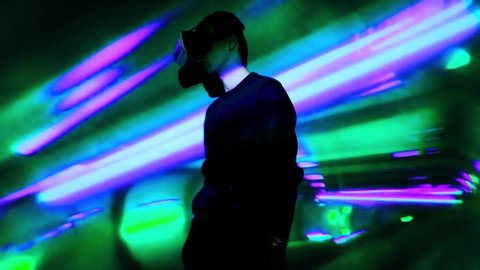 Young guy wave hands in front of display. Man watches and using VR-helmet virtual reality night at home. Portrait men at exhibition, club party with dynamic projector illumination. Large screen.