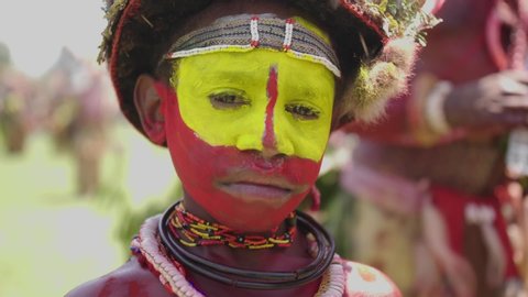 kanganama , Oceania / Papua New Guinea - 09 14 2019: Extreme close up focus shot, tribal boy face cover in red and yellow pain, other tribesmen’s in the background.