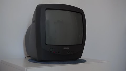 An old TV on a white wooden nightstand shows the noise and interference of the antenna. Old TV 90-2000 years old, stands on a white nightstand and shows the noise of the screen.