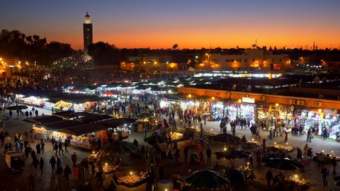 Crowds of people coming and going on Jemaa el-Fnaa marketplace of Marrakesh, Morocco just after sunset. Many counters with various goods. UHD