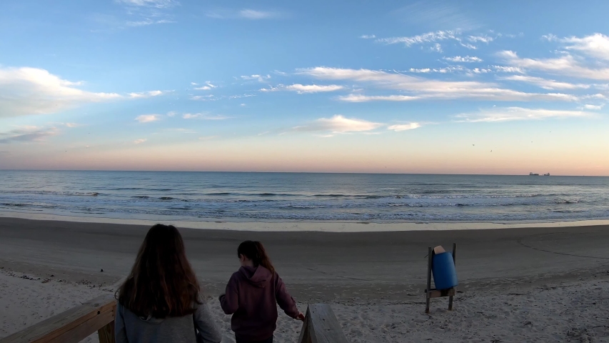 Looking over the top of twin girls moving down the stairs looking at the ocean at sunset, as wonderful colors illuminate the sky with a few clouds and deep blue color.