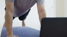 Asian man doing elbow plank up and down exercise in living room at home, watching live or video tutorial online via laptop computer. Activity during quarantine and social distance new normal concept.