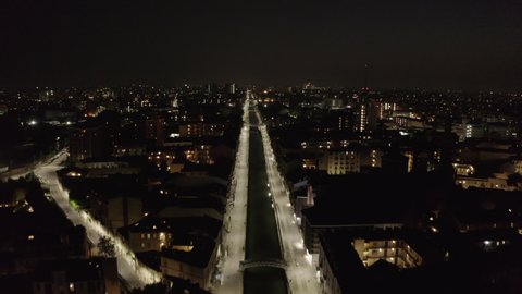 Aerial view of empty Navigli district in Milan, Italy with Naviglio Grande water canal from drone flying in the sky at night during coronavirus. Milano, Italian city and urban landscape with lights