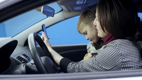 Brunette woman in casual clothes is driving car with greenscreen background. She is sitting in her car with her son on the bluesceen background isolated. She and her children are having a video chat