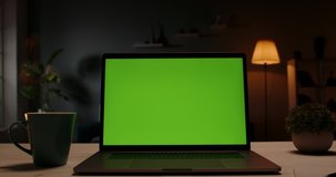 Chroma key green screen template - a laptop computer on a desk in cozy living room at night. Computer set for distance learning and remote work, technology concept 4k footage