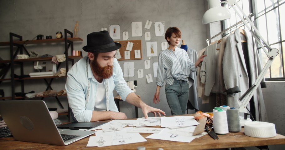 A hipster tailor couple is working together at their office, designing their new fashionable clothes collection - small family business concept 4k footage