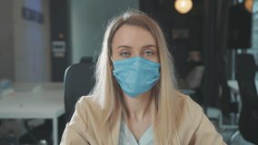 Serious young pretty woman removing facial respirator take break of extended mask wear looking at camera inside office corporate room. Business. Healthcare concept.