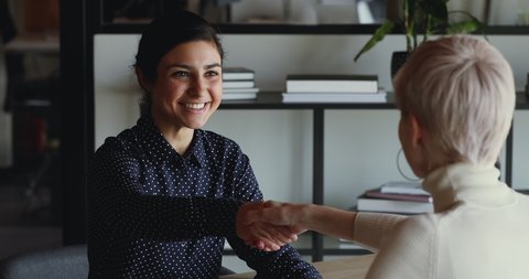 Happy confident indian recruit handshaking employer getting hired at new job. Smiling young female professional manager shake hand of woman client or customer making business deal at office meeting.