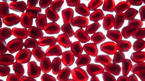 Red juice is flowing on the red grains of ripe pomegranate laying on the white shining background in slow motion