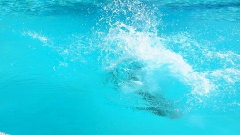 A boy in swimming goggles jumps rotating into a swimming pool. Splashes fly away