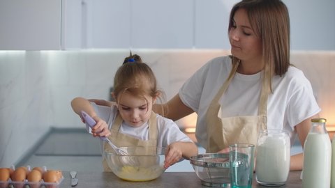 A preschool girl helps mom in the household with cooking. Loving mother teaches daughter to cook according to family recipes