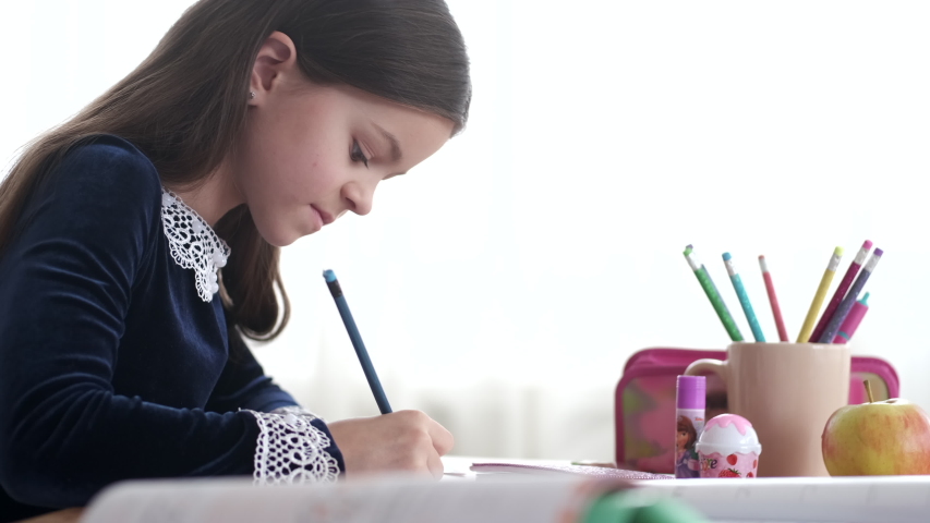 Pupil wears school uniform. Girl does writing exercises in notebook. Little girl does her homework.