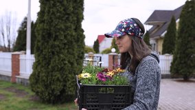A girl in a cap is carrying a basket of flowers to plant in the bedflower. Slow motion video